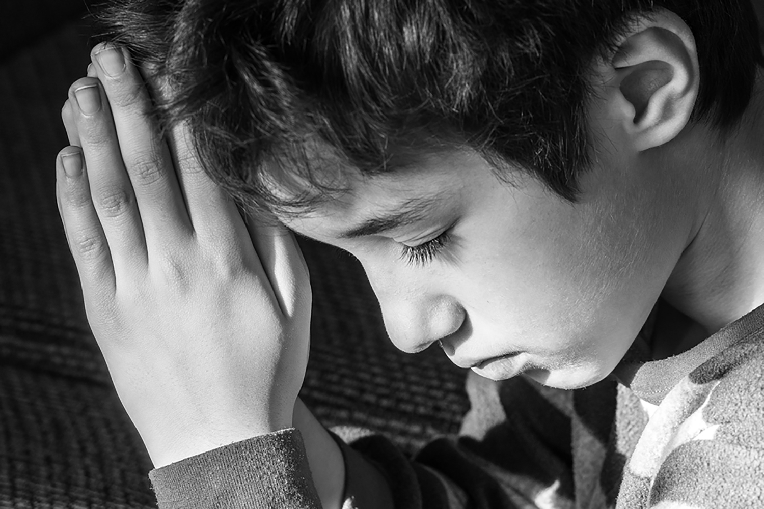 Young boy bowing his head and praying solemnly black and white Christian religious concept